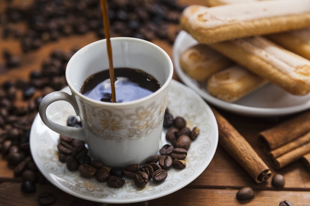 فنجان قهوه در کنار دانه های قهوه و چوب دارچین و نان